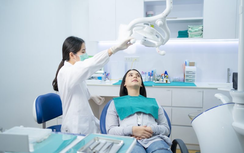 Asian female dentist adjust dental surgical light then start checking or examining tooth of patient